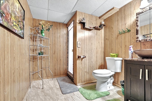 bathroom featuring vanity, wood walls, baseboards, and toilet