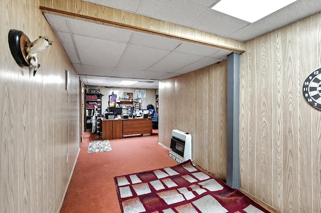 finished basement with carpet floors, heating unit, wooden walls, and a paneled ceiling
