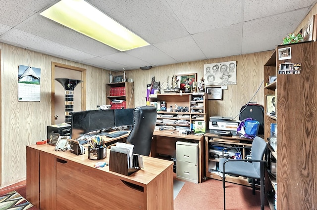 carpeted home office featuring wood walls and a paneled ceiling