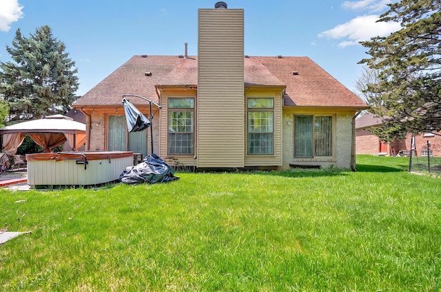rear view of house with roof with shingles, a chimney, brick siding, a hot tub, and a yard