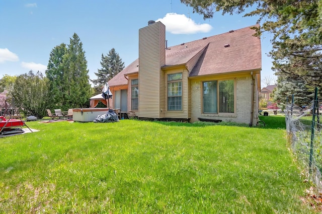 back of house with a chimney, roof with shingles, a lawn, brick siding, and fence