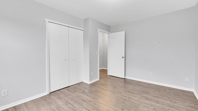 unfurnished bedroom featuring baseboards, wood finished floors, and a closet