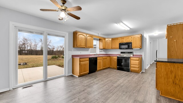 kitchen featuring dark countertops, light wood-style flooring, a ceiling fan, visible vents, and black appliances