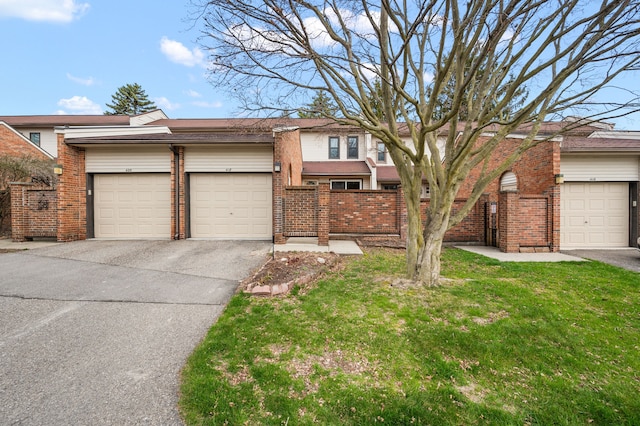 view of front of house featuring an attached garage, a front yard, aphalt driveway, and brick siding