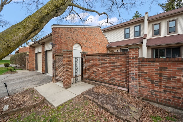 exterior space featuring fence, an attached garage, driveway, and brick siding