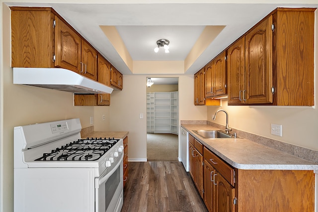 kitchen featuring brown cabinetry, a sink, under cabinet range hood, and white appliances