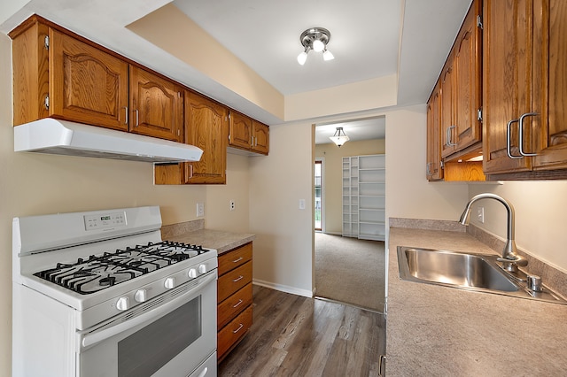 kitchen featuring a sink, light countertops, brown cabinetry, under cabinet range hood, and white range with gas cooktop