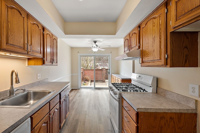 kitchen featuring white appliances, under cabinet range hood, brown cabinets, a sink, and light wood-style flooring