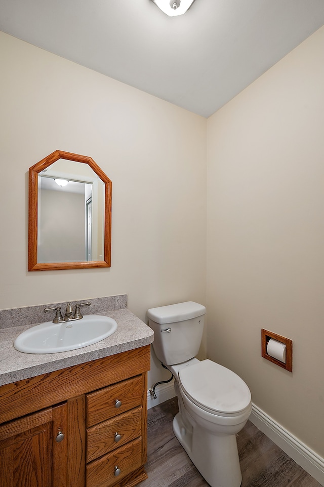 half bath with baseboards, vanity, toilet, and wood finished floors