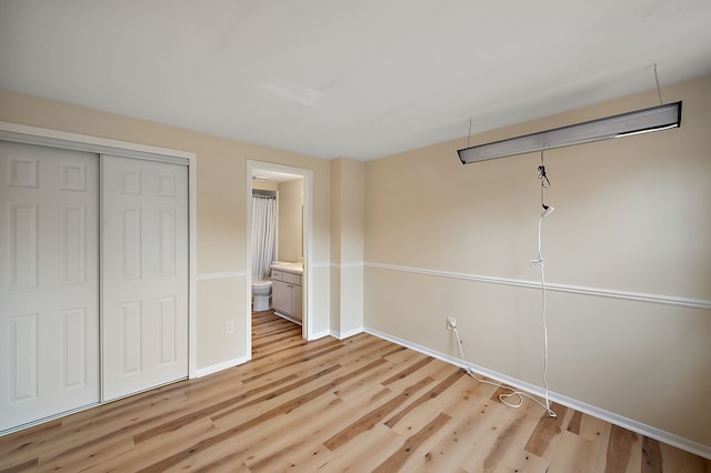 unfurnished bedroom with a closet, baseboards, ensuite bathroom, and light wood-style floors