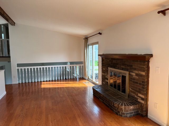 living room with baseboards, a brick fireplace, wood finished floors, and beamed ceiling