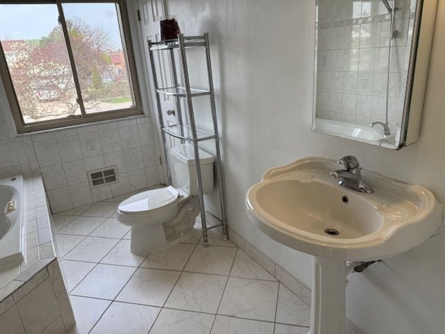bathroom featuring tiled bath, a sink, toilet, tile patterned floors, and visible vents