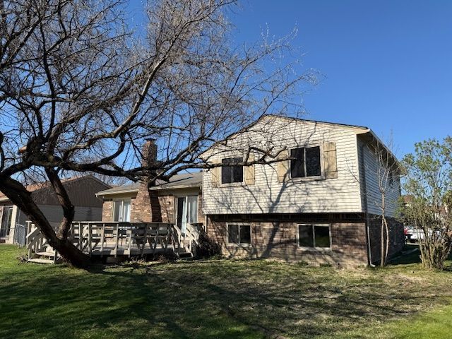 view of front of house featuring brick siding, a deck, a chimney, and a front lawn
