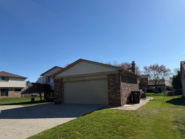 view of side of home with a yard, brick siding, an attached garage, and decorative driveway