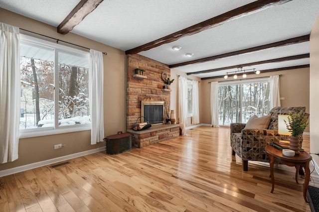 living room featuring visible vents, beam ceiling, baseboards, a stone fireplace, and a textured ceiling