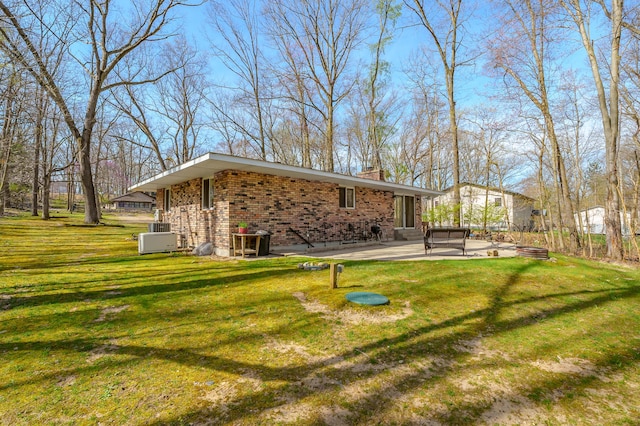 back of property featuring brick siding, a patio, a yard, and a chimney