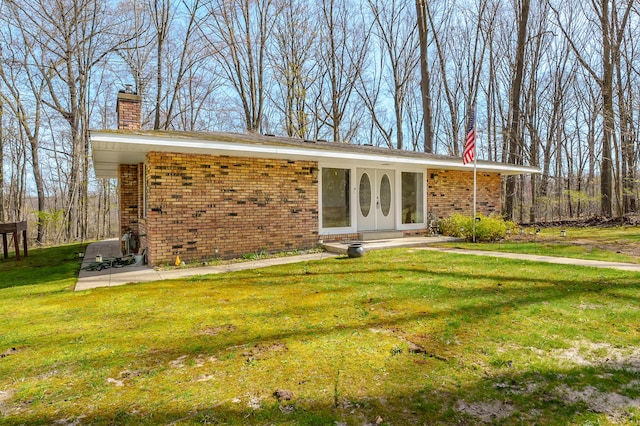 rear view of property with a lawn, brick siding, and a chimney