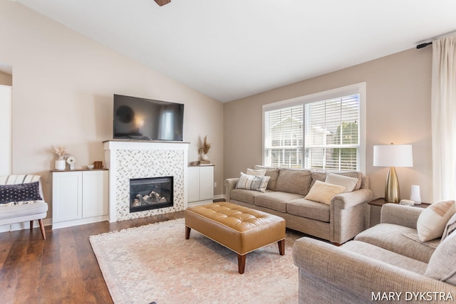 living room with a tiled fireplace, vaulted ceiling, and dark wood finished floors