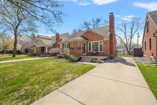 view of front facade featuring fence, brick siding, a front yard, a chimney, and driveway