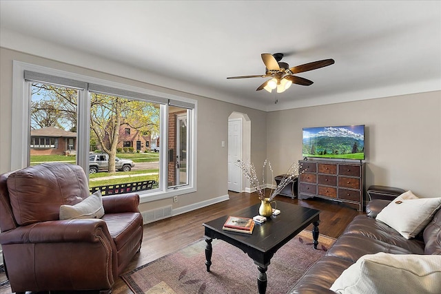 living room featuring dark wood-style flooring, ceiling fan, arched walkways, baseboards, and visible vents