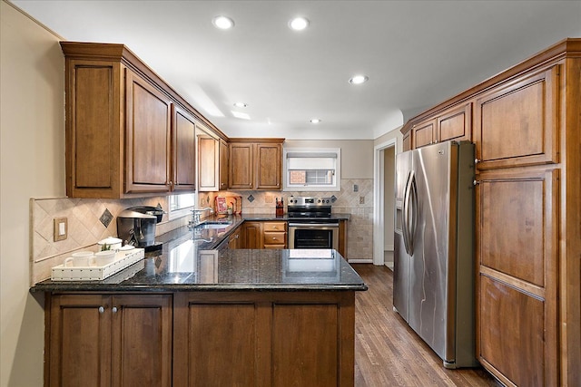 kitchen with a peninsula, wood finished floors, dark stone counters, a sink, and stainless steel appliances