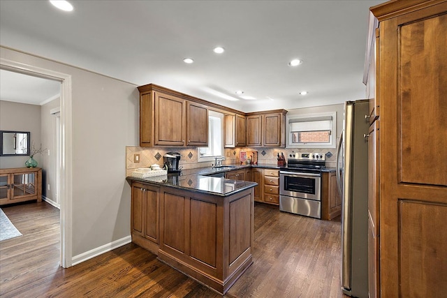kitchen featuring brown cabinetry, dark countertops, a peninsula, stainless steel appliances, and dark wood-type flooring