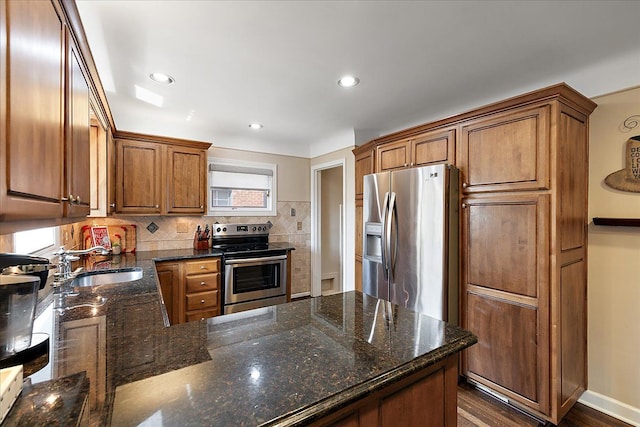 kitchen featuring dark stone counters, brown cabinets, tasteful backsplash, a sink, and stainless steel appliances