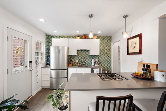 kitchen featuring a peninsula, wood finished floors, a kitchen bar, white cabinetry, and stainless steel appliances