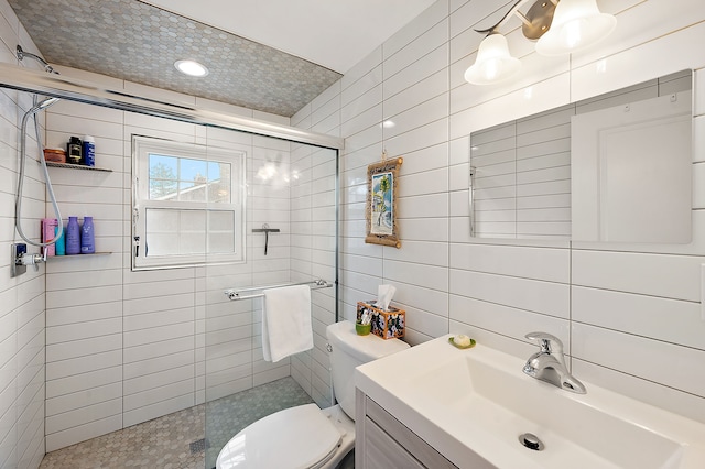 full bathroom with vanity, a tile shower, toilet, and tile walls