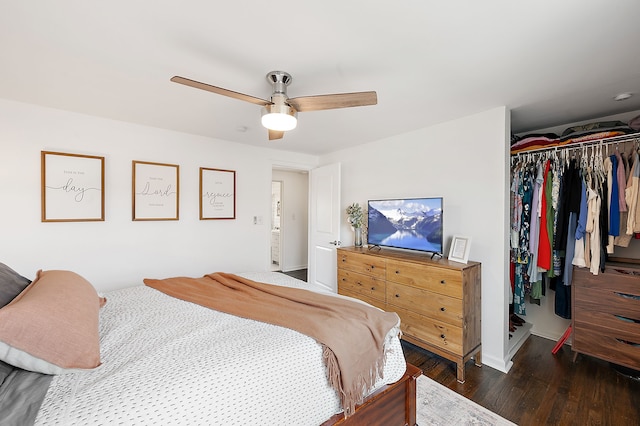 bedroom with a closet, wood finished floors, baseboards, a spacious closet, and a ceiling fan