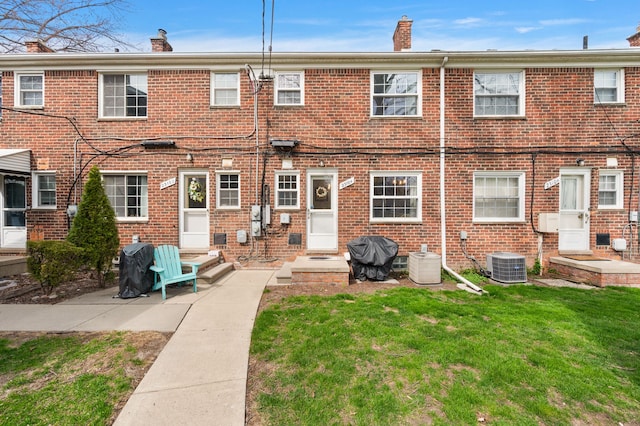 rear view of property featuring brick siding, central AC unit, a yard, and a chimney