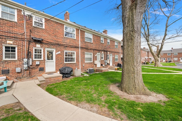 rear view of property with a yard, brick siding, and a chimney
