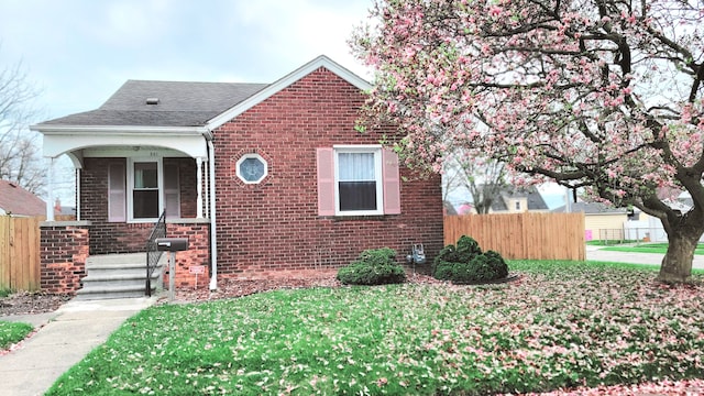 bungalow featuring brick siding and fence