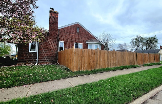 view of side of home with fence, a chimney, a yard, and brick siding