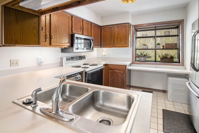 kitchen with light countertops, brown cabinets, a sink, light tile patterned floors, and stainless steel appliances