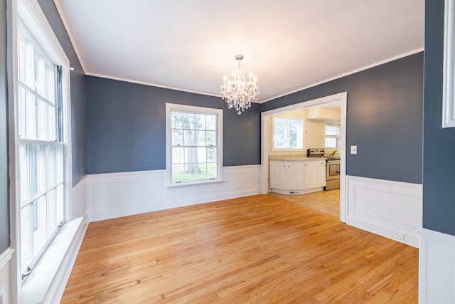 unfurnished dining area featuring an inviting chandelier, ornamental molding, a decorative wall, a wainscoted wall, and light wood finished floors