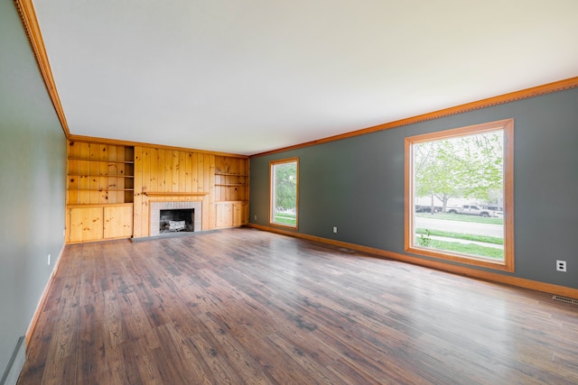 unfurnished living room with baseboards, ornamental molding, a brick fireplace, and wood finished floors