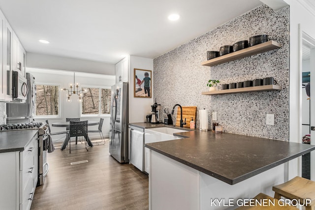 kitchen with backsplash, dark countertops, a sink, stainless steel appliances, and white cabinetry