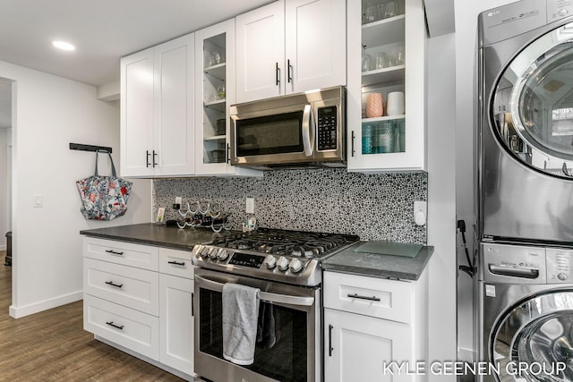 kitchen featuring stacked washer and clothes dryer, dark countertops, dark wood finished floors, backsplash, and stainless steel appliances