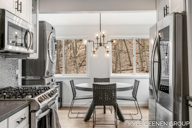 kitchen featuring plenty of natural light, dark countertops, appliances with stainless steel finishes, baseboards, and stacked washer and clothes dryer