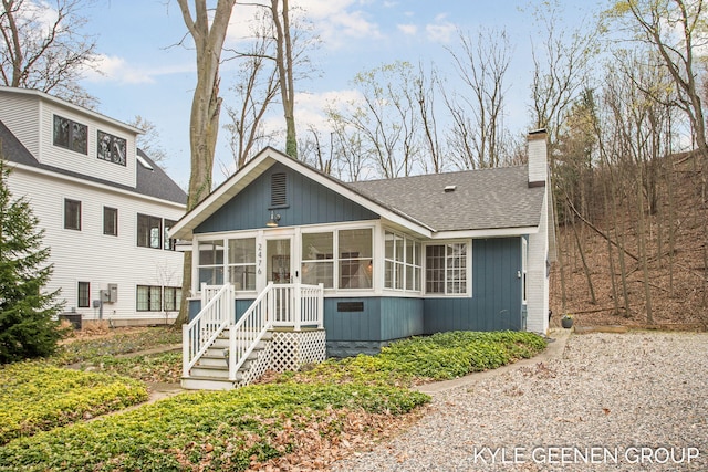 rear view of property featuring roof with shingles, a chimney, and a sunroom
