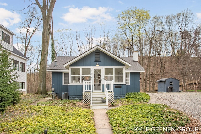 bungalow-style house with a storage unit, a shingled roof, a sunroom, a chimney, and an outdoor structure