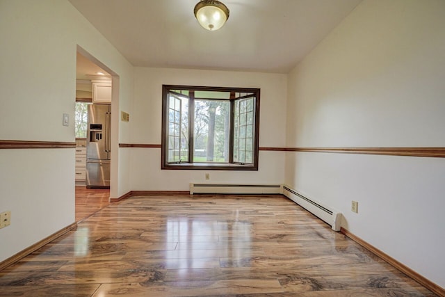 empty room featuring baseboards, a baseboard heating unit, and wood finished floors