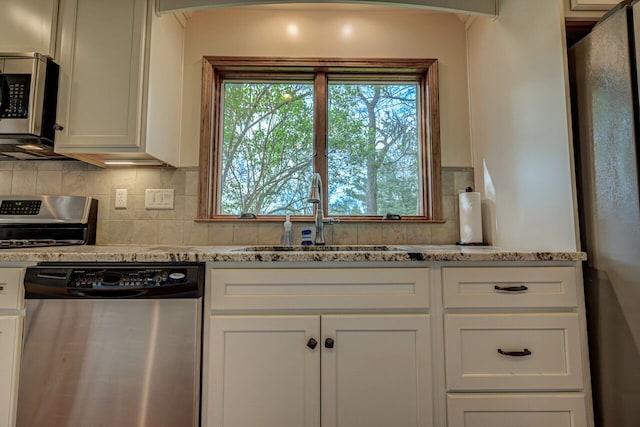 kitchen with stainless steel appliances, light stone countertops, a sink, and tasteful backsplash