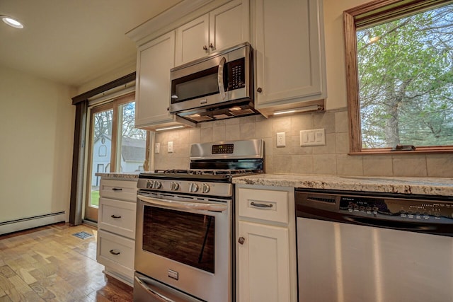 kitchen featuring appliances with stainless steel finishes, backsplash, light wood-type flooring, and light stone counters