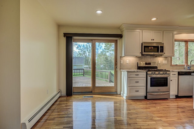 kitchen featuring baseboard heating, stainless steel appliances, light wood finished floors, and white cabinetry