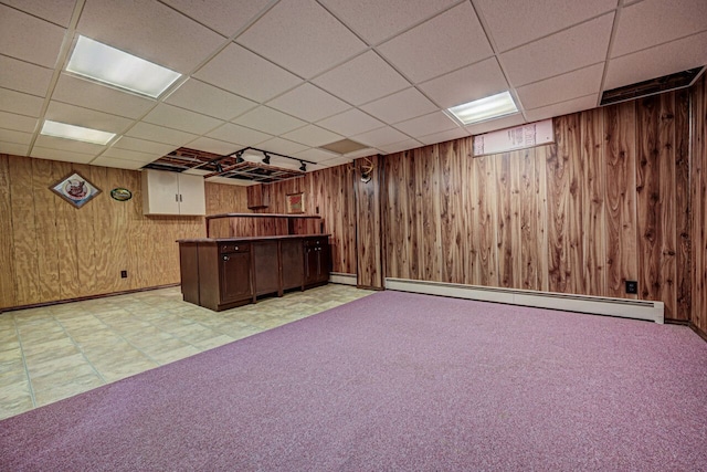 below grade area featuring wooden walls, tile patterned floors, a drop ceiling, and a baseboard heating unit