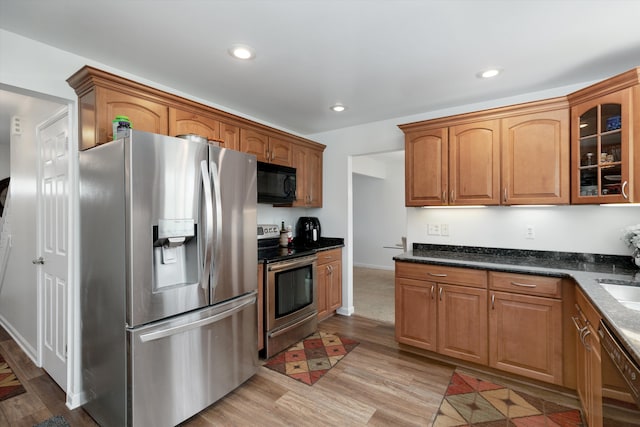 kitchen with light wood-style floors, brown cabinetry, black appliances, glass insert cabinets, and recessed lighting