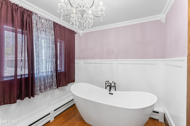 bathroom with crown molding, baseboard heating, a notable chandelier, a soaking tub, and a decorative wall