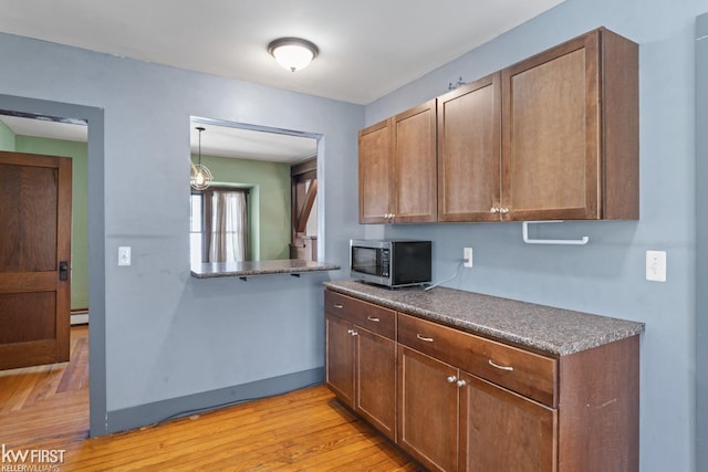 kitchen with dark countertops, light wood-style floors, brown cabinetry, stainless steel microwave, and a baseboard radiator